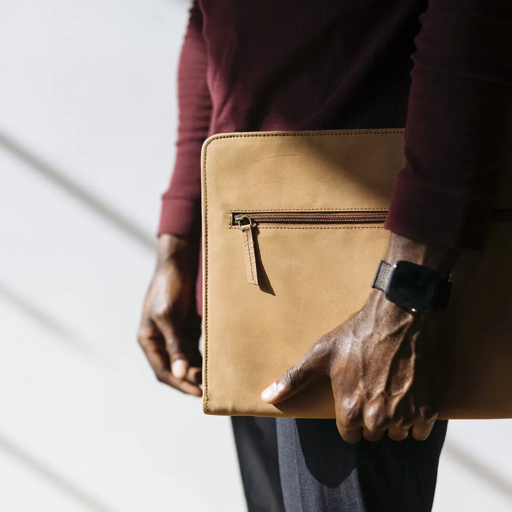 Man in maroon long sleeve with black watch holding a beige Notary Bag
